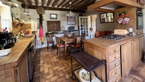 A rustic kitchen with wooden beams, a herringbone floor, a central island with a gas stove, and a dining area with chairs and a table. - A pastoral setting within reach of seaside (12-25 kms) - Sleeps 6-8 (Manneville-La-Raoult)