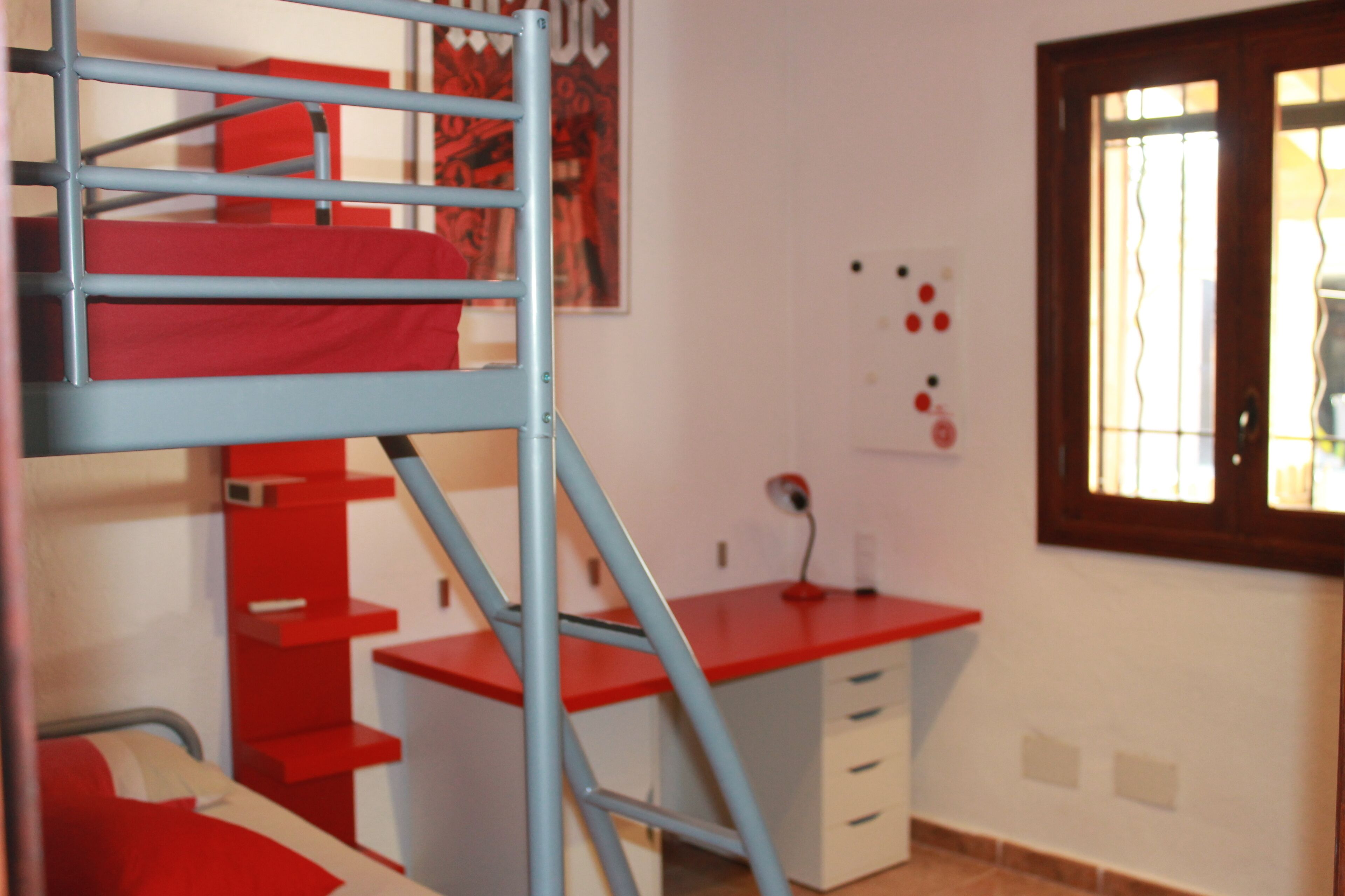 A room with a bunk bed, a desk with drawers, a chair, and a window with curtains.