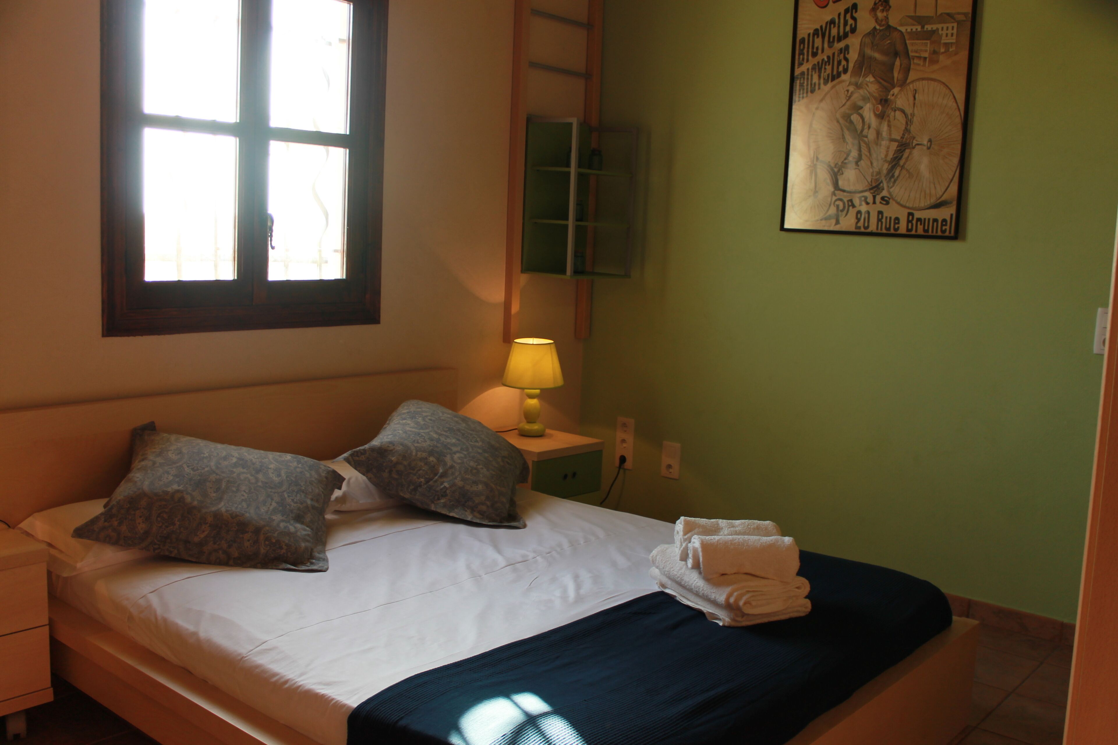 A bedroom with a bed, pillows, a nightstand, a lamp, a poster on the wall, and a window.