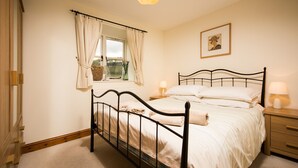 A bedroom with a single bed, a nightstand, a window with curtains, a bedside lamp, and a framed picture on the wall.