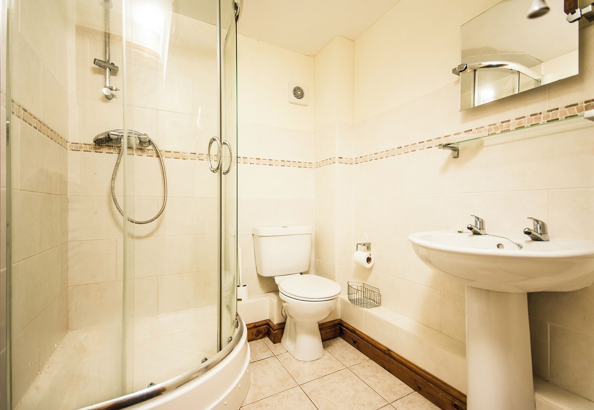 Une salle de bain avec une douche à parois de verre, des toilettes blanches et un lavabo sur colonne.