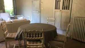 Uma área de refeições com uma mesa redonda, quatro cadeiras, um radiador e uma porta ao fundo.