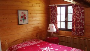 Una habitación de madera con una cama, una mesa con lámpara y una ventana con cortinas.