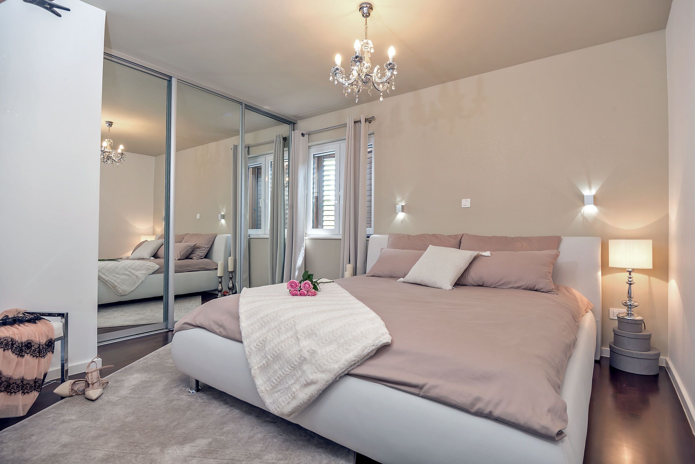 A bedroom with a large bed, a chandelier, a bedside lamp, and a mirror.