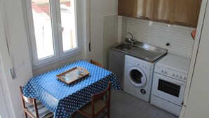 Una cocina pequeña con lavadora, un lavamanos y una mesa con mantel de lunares.