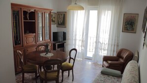 Una sala de estar con una mesa de comedor, sillas, un sofá, un televisor y un armario.
