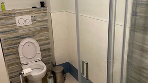 Un baño moderno con cabina de ducha de vidrio, un inodoro con dispensador de toallas de papel y un cubo de basura.