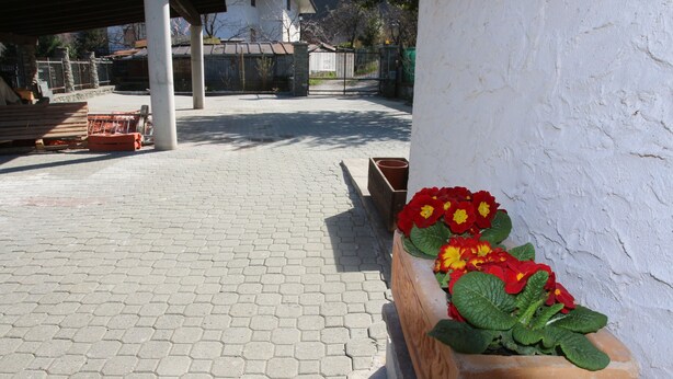 Une cour dallée avec des carreaux hexagonaux, un banc en bois et des jardinières ornées de fleurs rouges et jaunes.