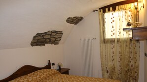 Une chambre à coucher avec un lit, une tête de lit en bois, un mur en pierre, un radiateur et une fenêtre avec des rideaux.
