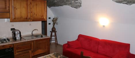Una cuina amb armaris de fusta, un sofà vermell i una paret de pedra.