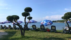 A beachside seating area with rows of chairs and umbrellas, a clear view of the sea, and neatly trimmed trees. - Umag Savudrija Vacation Home, near the beach, balcony, Wi-Fi (Bašanija)