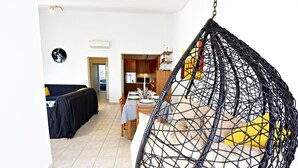 A modern living room with a hanging chair, a dining area with a table set for two, and a kitchen in the background. - Umag Savudrija Vacation Home, near the beach, balcony, Wi-Fi (Bašanija)
