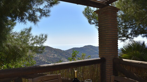 Une terrasse en bois avec une bouteille de vin et des verres, offrant une vue sur un paysage montagneux.