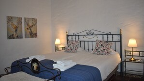 Un lit bien fait, avec une couvre-lit bleue et du linge de lit blanc, deux coussins décoratifs, un climatiseur fixé au mur et deux lampes fixées au mur.