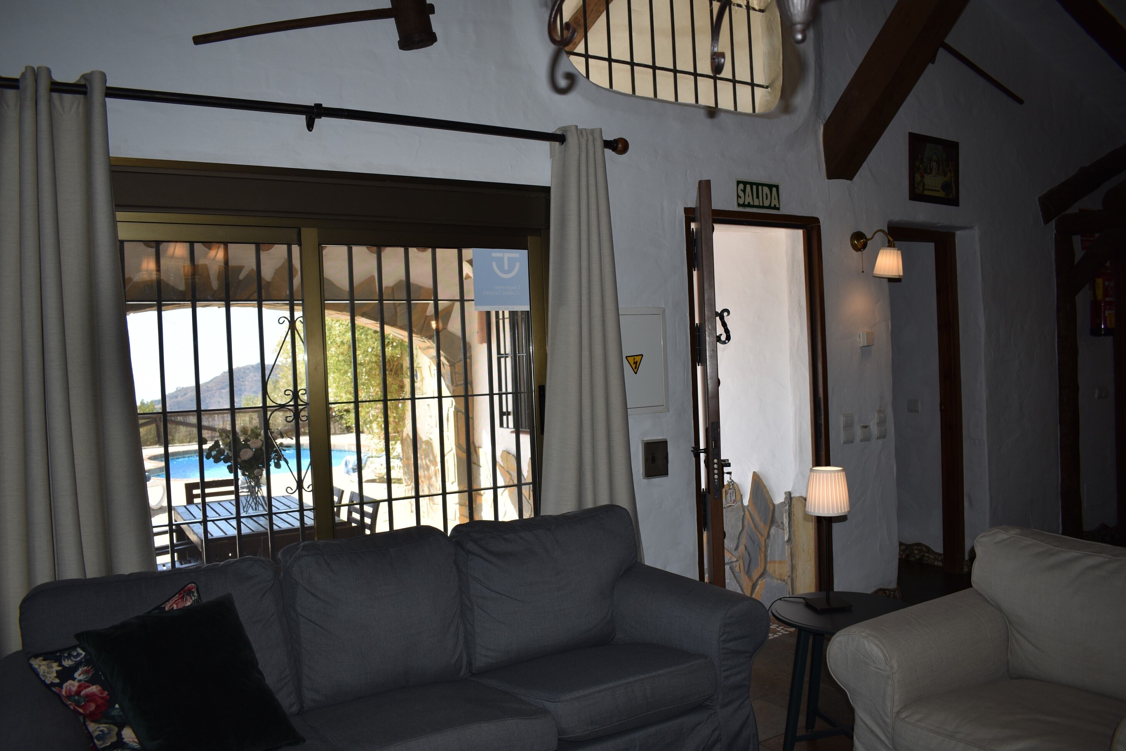 A living room with a sofa, a lamp, and a view of a pool through a barred window.
