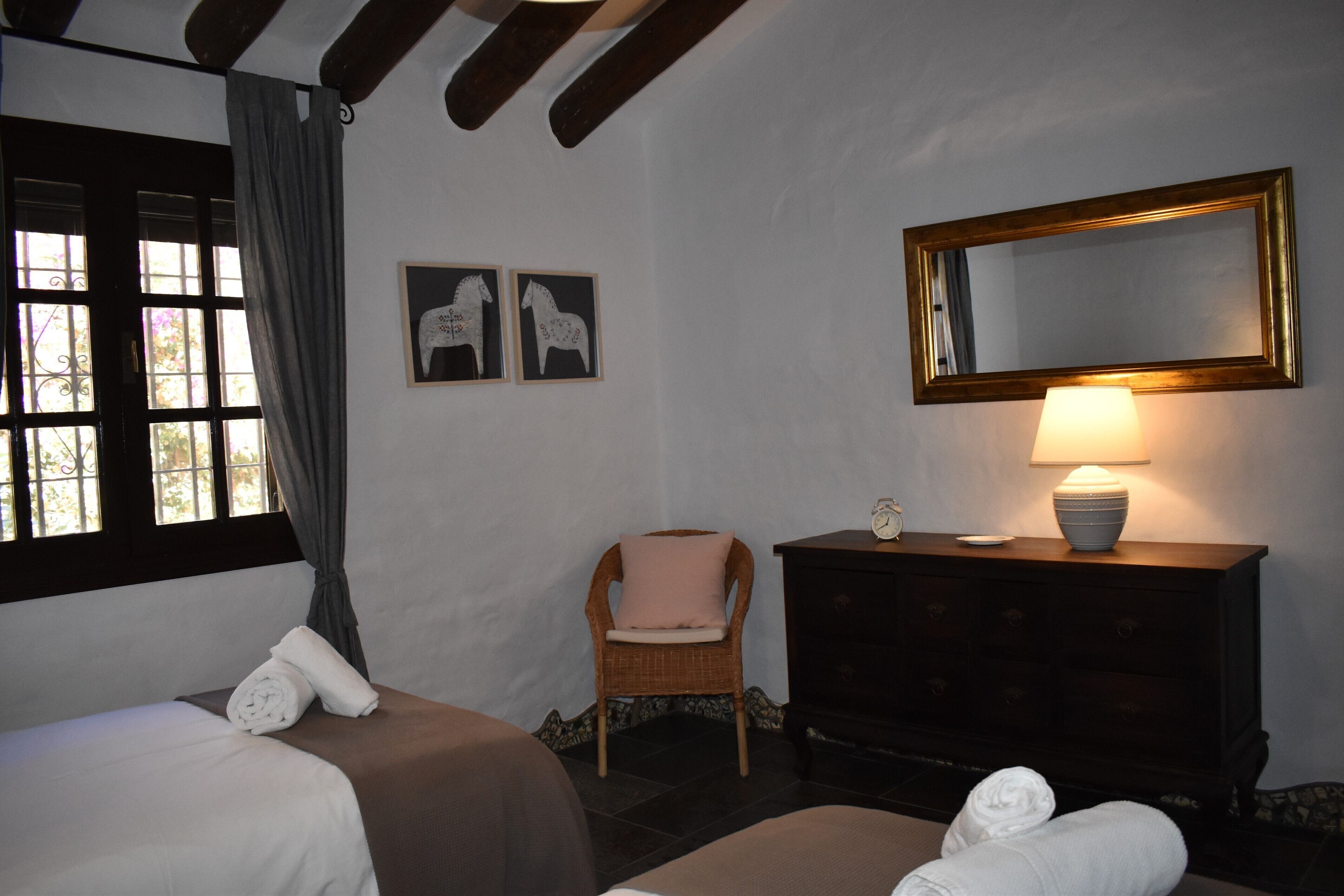 A room with two beds, a chair, a dresser, a mirror, and two framed pictures on the wall.