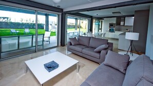 A modern living room with a white coffee table, a grey sofa, and a glass door leading to a patio with outdoor furniture.