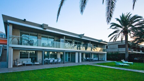 A modern building with a flat roof, large windows, and a covered outdoor seating area with chairs and tables.