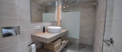 A modern bathroom with a large mirror, a round sink, a glass shower enclosure, and a wooden vanity.