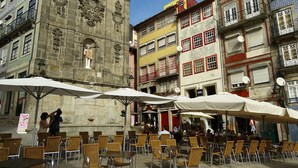 Uma praça com mesas ao ar livre e um edifício histórico com trabalhos em pedra ornamentados.