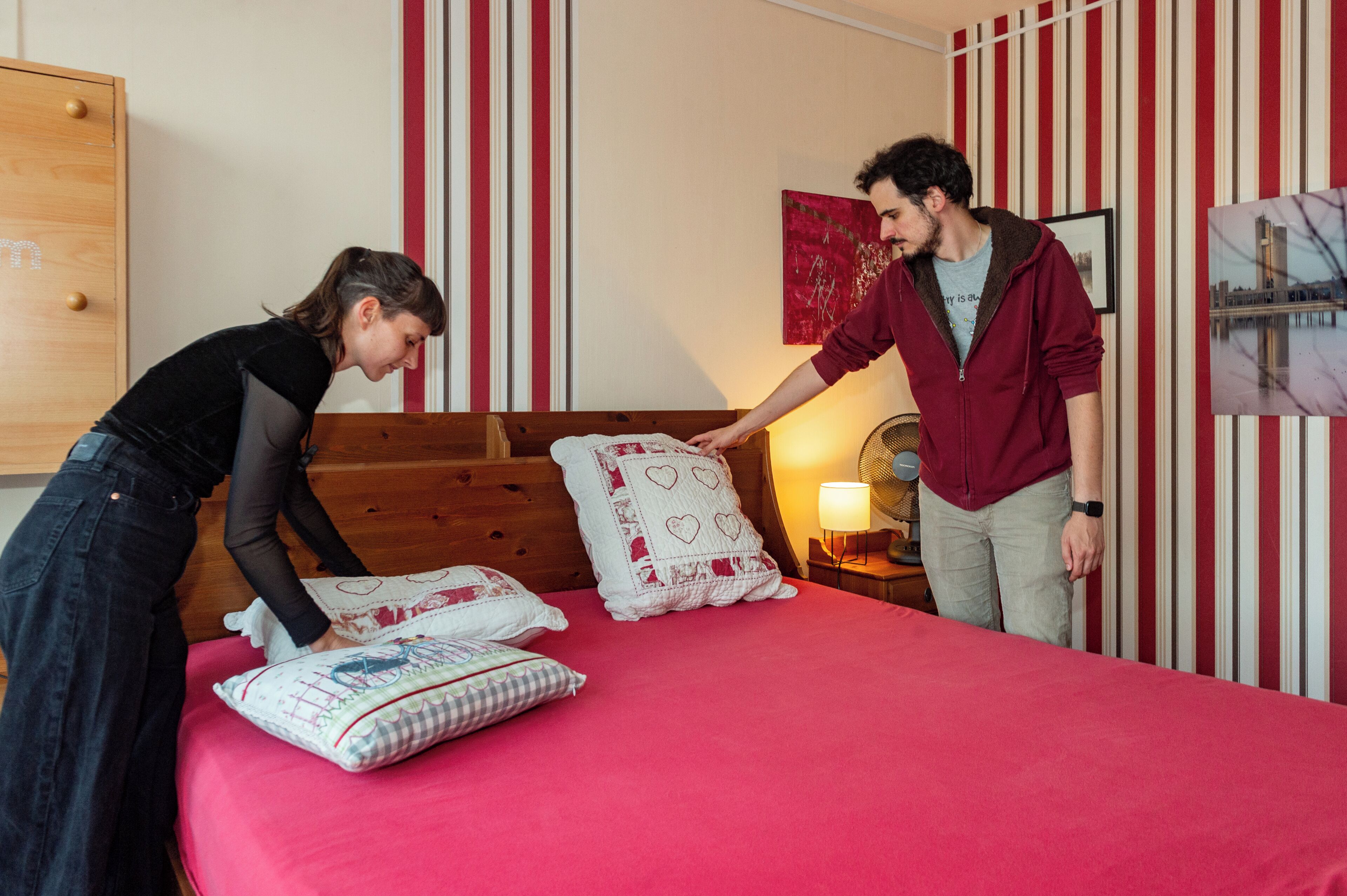 Een slaapkamer met een houten hoofdbord, een rode sprei en gestreept behang.