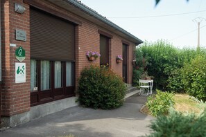 A brick building with a closed garage door, a sign indicating a location, and a small outdoor seating area with a table and chairs.