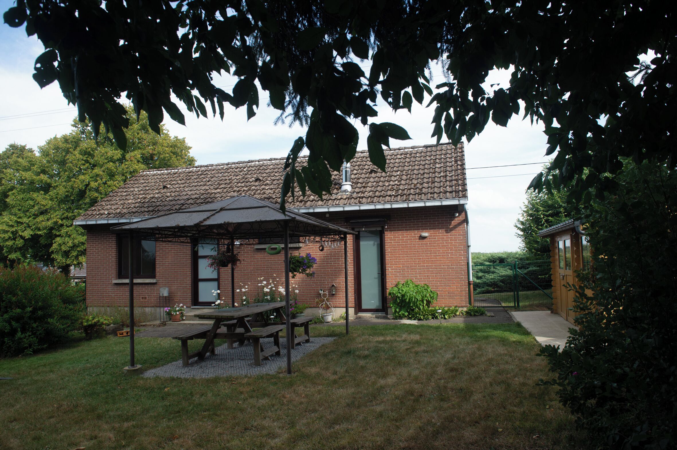 A brick building with a covered patio, a picnic table, and a small garden area.