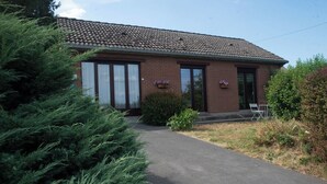A single-story brick building with a tiled roof, a covered driveway, and a small garden area with shrubs and flowers.