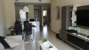 Un soggiorno moderno con divano, tavolino e mobile TV. Si intravede in secondo piano una cucina con tavolo e sedie.