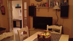 A dining area with a table set for four, a basket of apples, a clock, and a television on the wall. - La Cuesta Blanca House or chalet (Castilla de la Mancha)