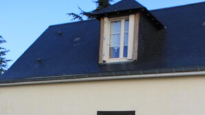 A building with a dark roof, a beige wall, and a wooden door with shutters. There is a small potted plant near the door and a fish-shaped sign on the wall. - Les Pins at La Cerniére with shared pool (Deneze sous Le Lude)