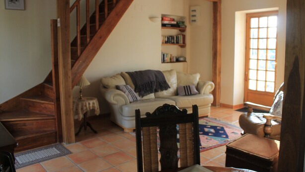 A cozy living room with a staircase, a sofa, a bookshelf, and a window. - Les Pins at La Cerniére with shared pool (Deneze sous Le Lude)