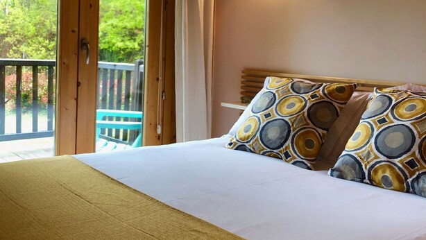 Un dormitorio con cama, almohadas, una mesita de noche, una ventana con cortinas y vistas a zonas verdes.