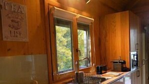Interior de madera con cocina, que incluye un lavamanos, armarios y una ventana con vista a la vegetación.