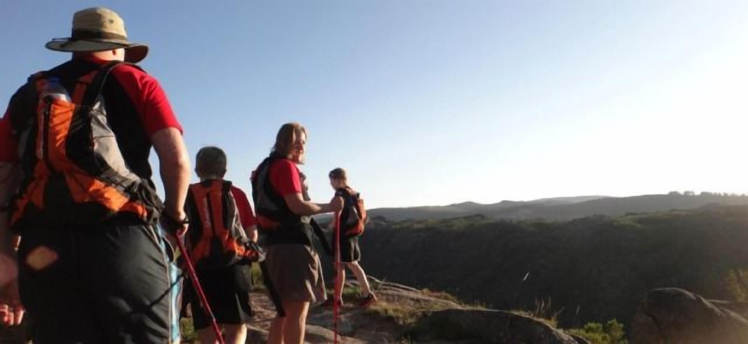 Un grupo de personas caminando por un sendero con mochilas, rodeado de paisaje natural.