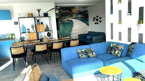 A modern living space with a blue sofa, wicker chairs, a dining area, and a large wall mural.