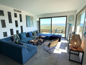 A modern living room with a blue sofa, a wicker chair, and a dining area with a table and chairs.