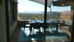 A balcony with a table set for dining, overlooking a scenic landscape with mountains and a body of water.