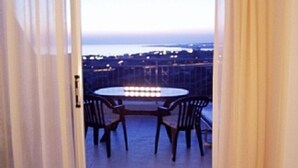 Un balcon ouvert avec une table ronde et deux chaises, donnant sur une vue panoramique de la ville au crépuscule.