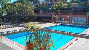 Una piscina con solárium de baldosas, rodeada de plantas en macetas y árboles.