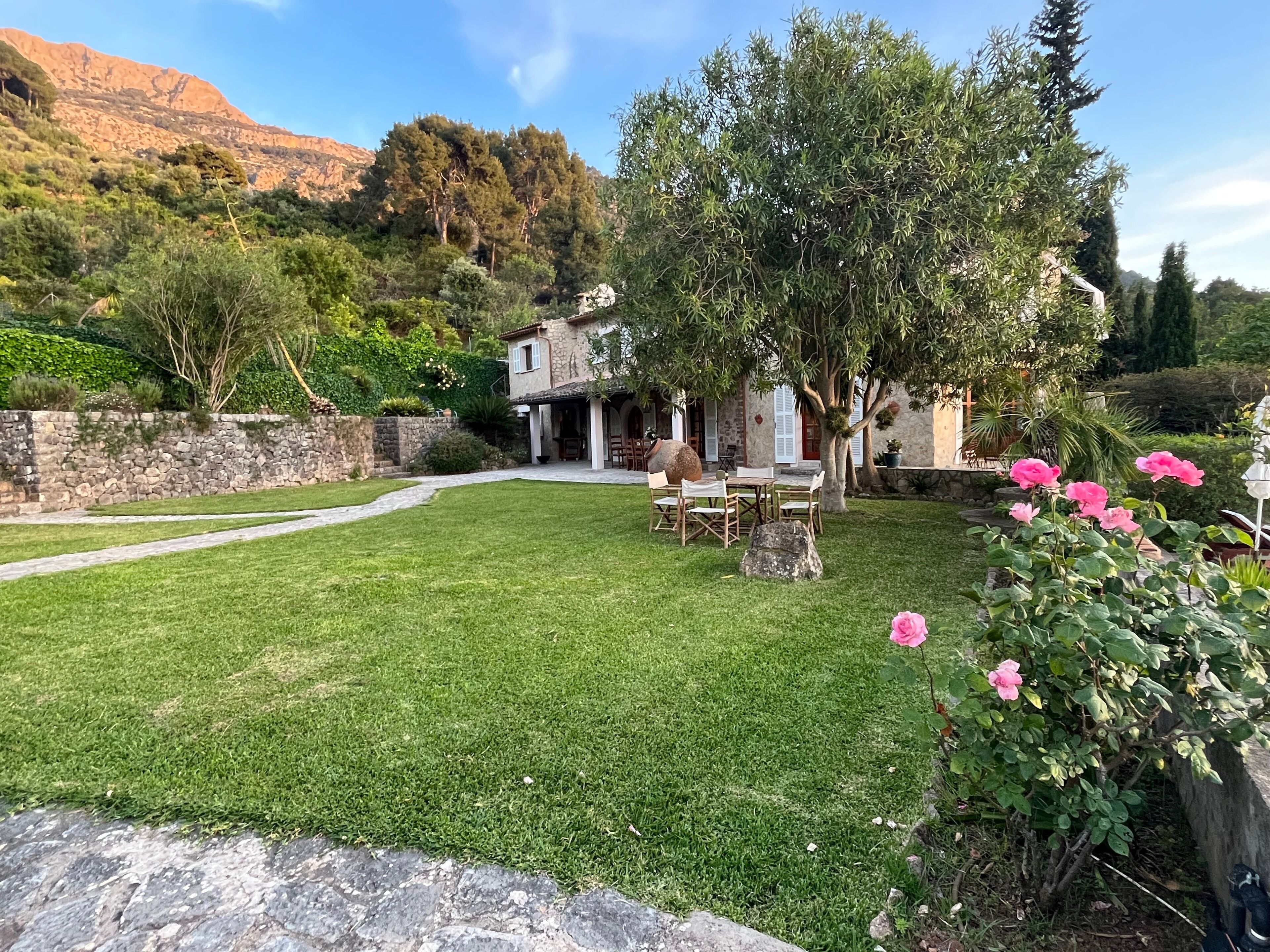 A stone house with a patio, surrounded by a well-maintained lawn and a stone wall.