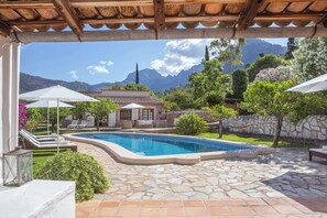 A pool area with lounge chairs and umbrellas, surrounded by stone walls and greenery, with mountains in the background. - Beautiful Country Villa With Private Pool & Huge Garden (Sóller)