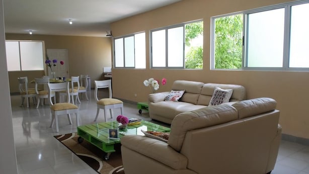 Una sala de estar con un sofá color beige, una mesa de centro de vidrio y un comedor con sillas blancas y una mesa.