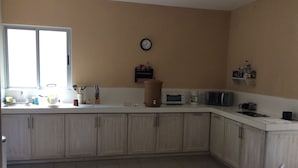Una cocina con ventana, reloj, microondas, tostadora y armarios.