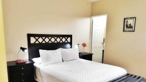 Una cama bien hecha con cabecera de madera, una mesita de noche con lámpara y un banco al pie de la cama.