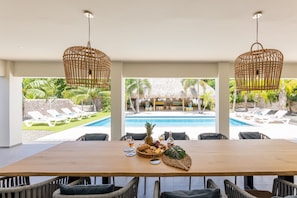 A dining area with a wooden table, wicker chairs, and a view of a pool and outdoor seating area.