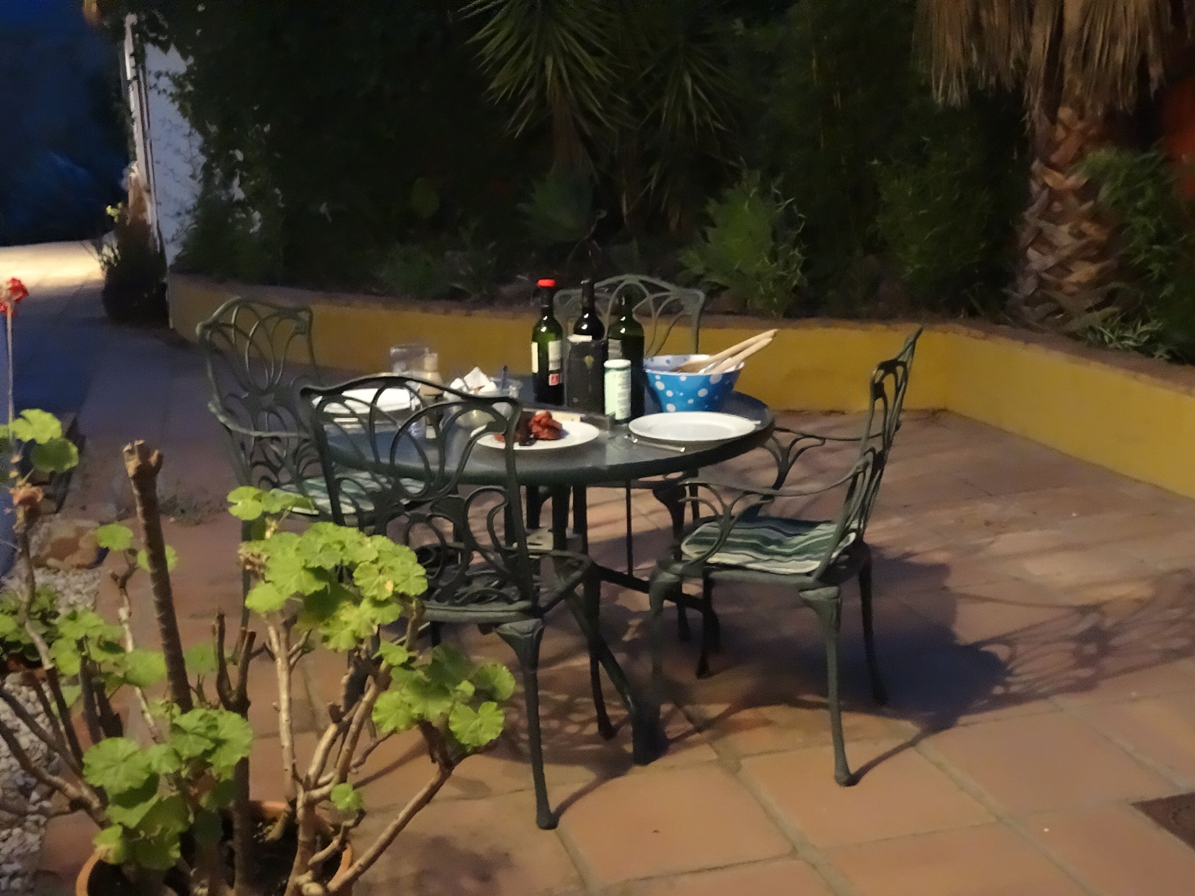 En udendørs patio med et rundt bord og stole, omgivet af planter og en gul væg.