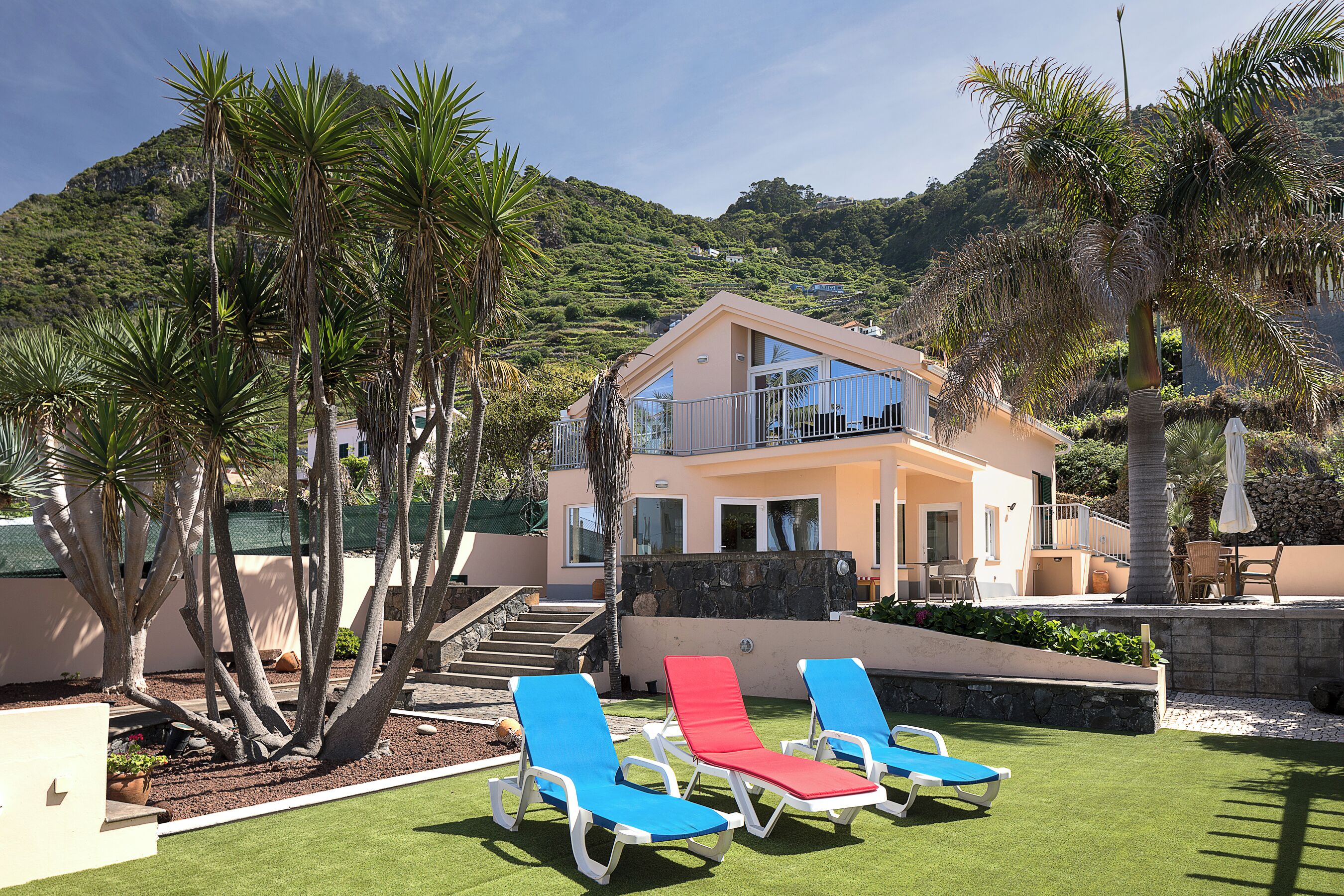 A two-story house with a balcony, surrounded by palm trees and a well-maintained lawn.