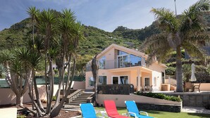 Une maison à deux étages dotée d’un balcon, entourée de palmiers et d’une pelouse bien entretenue.
