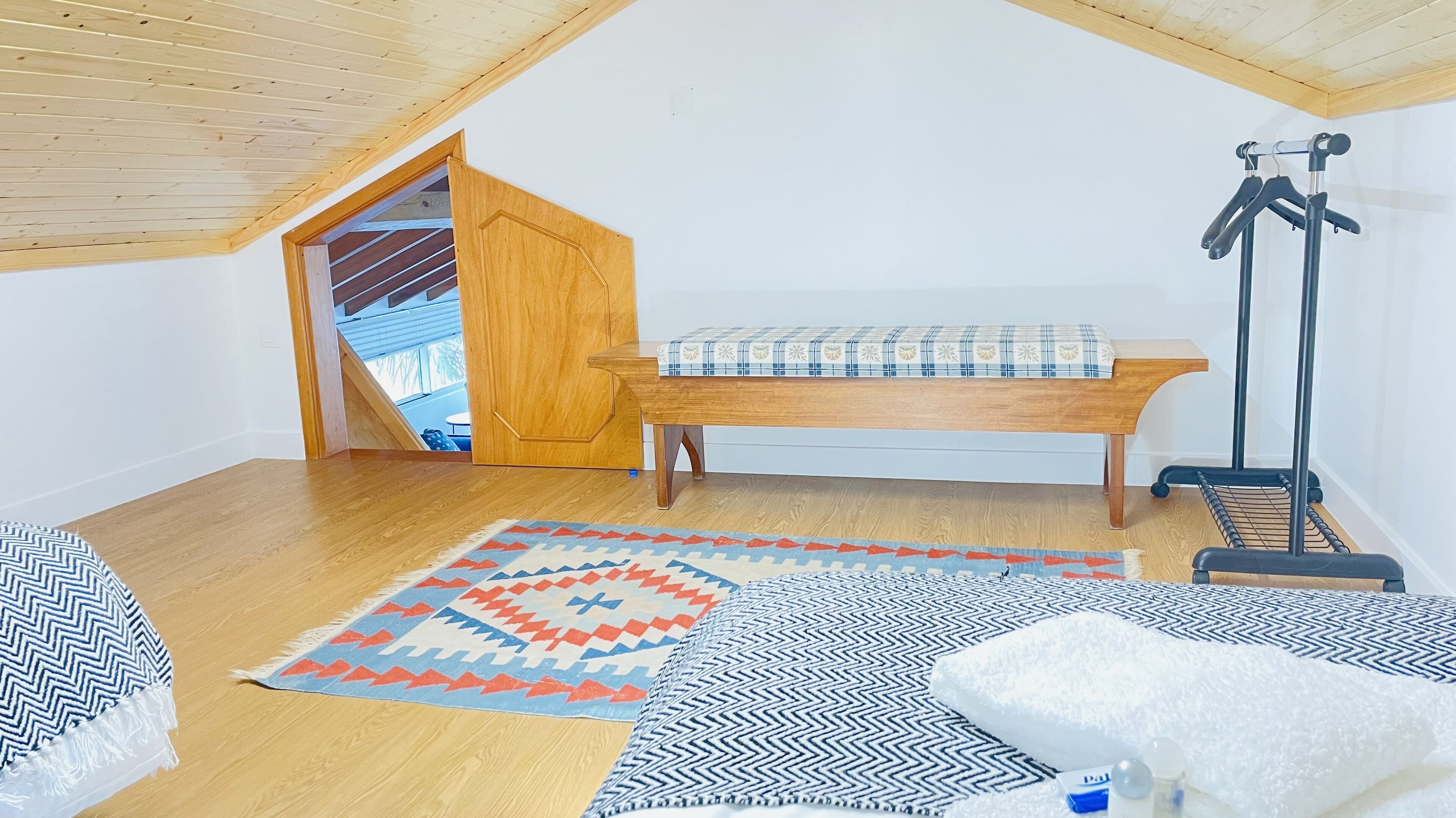 Slaapkamer met hoge plafonds, een houten bank, een kapstok en een vloerkleed met patroon.